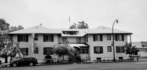 A snow-covered building with multiple windows and a flag, surrounded by trees, captured in black and white.