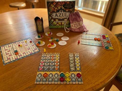 A tabletop game setup of Azul, featuring colorful tiles, player boards, and game pieces on a wooden table.