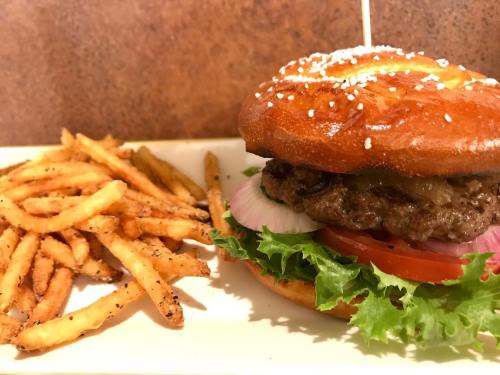 A juicy burger with lettuce, tomato, and onion on a sesame seed bun, served with a side of crispy fries.