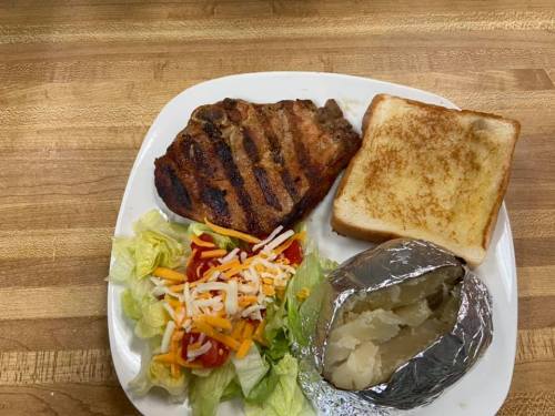 A plate with grilled meat, a baked potato in foil, toast, and a salad with lettuce, cheese, and tomato.