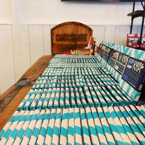 A display of neatly arranged chocolate bars on a wooden table, with a sign reading "CHOCOLATE" in the background.