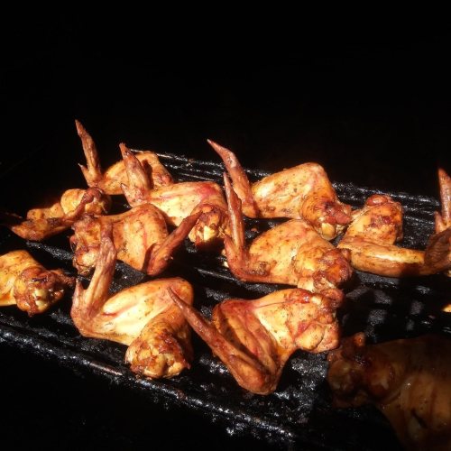 Grilled chicken wings sizzling on a barbecue grill, coated in a rich, golden marinade.