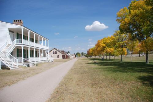 A historic building along a dirt path lined with trees, showcasing vibrant autumn colors under a blue sky.