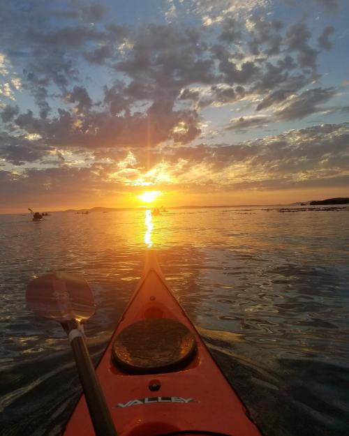A kayak on calm water at sunset, with vibrant clouds and reflections in the water.