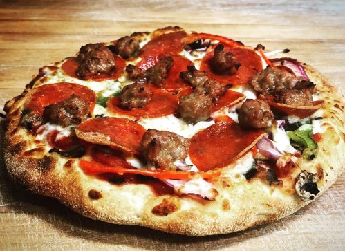 A freshly baked pizza topped with pepperoni, sausage, and vegetables on a wooden surface.