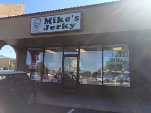 Exterior of Mike's Jerky store with a sign, open door, and large windows displaying jerky promotions.