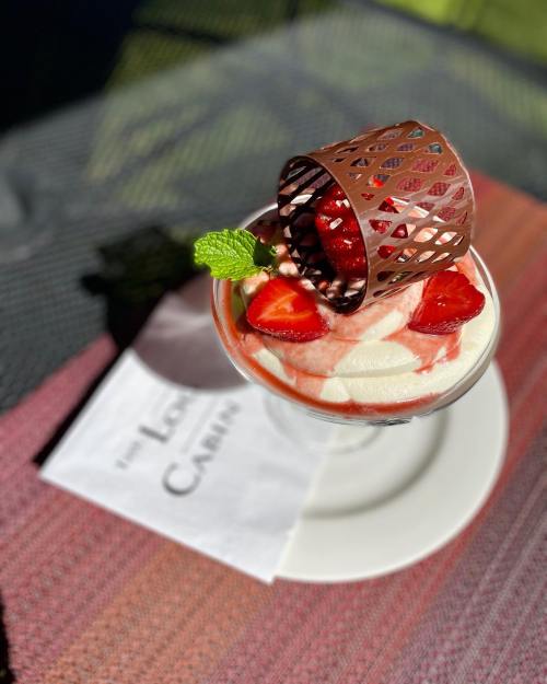 A dessert glass filled with whipped cream, strawberries, and a decorative chocolate piece, served on a colorful tablecloth.