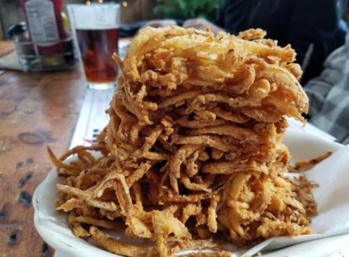 A large pile of crispy, golden-brown fried onions on a plate, with a blurred background of a restaurant setting.
