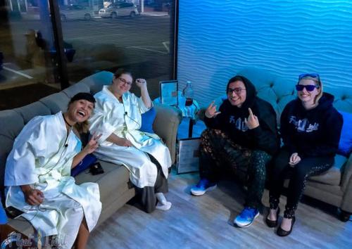 Four people in cozy robes sit together in a relaxed setting, smiling and posing for the camera.