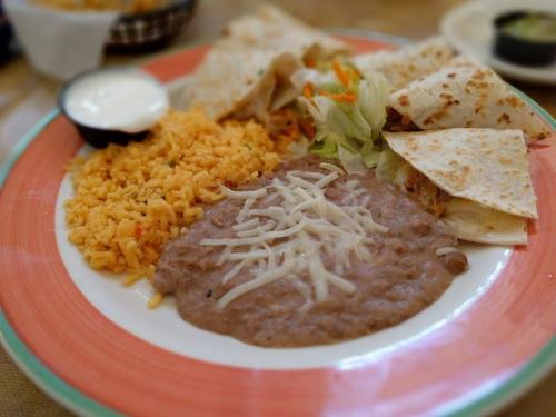 A colorful plate featuring rice, refried beans topped with cheese, tortillas, and a side of salad.