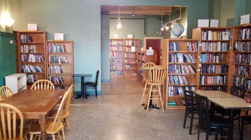 A cozy library interior with wooden bookshelves, tables, and chairs, filled with books and warm lighting.