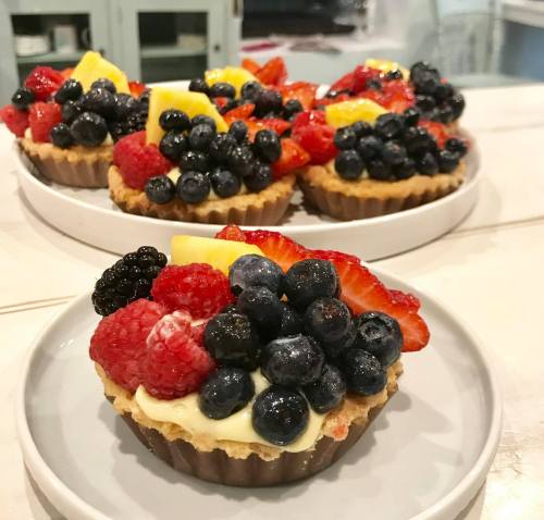 Colorful fruit tarts topped with blueberries, raspberries, strawberries, and lemon slices on a white plate.