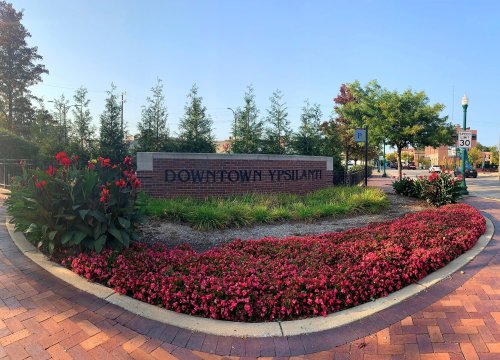 Sign for Downtown Ypsilanti surrounded by colorful flowers and greenery on a sunny day.