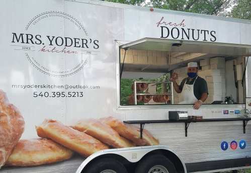 A food truck named "Mrs. Yoder's Kitchen" serves fresh donuts, with a smiling vendor holding a donut at the window.