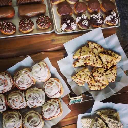 A variety of baked goods including donuts, cinnamon rolls, and cookie bars displayed on wooden surfaces.