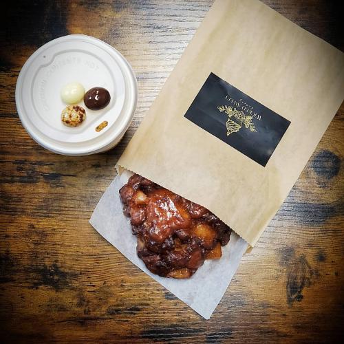 A paper bag with a warm pastry and a cup of assorted chocolates on a wooden table.