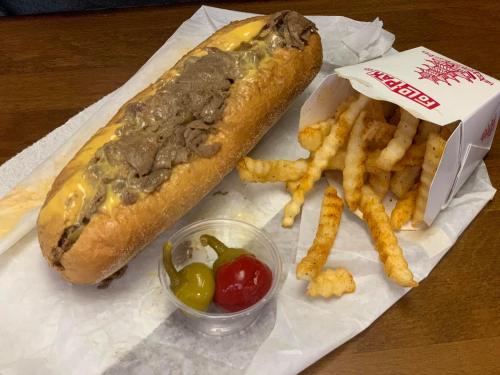 A cheesesteak sandwich with melted cheese, served with crinkle-cut fries and a side of pickled peppers.
