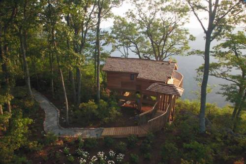 A wooden treehouse nestled among trees, with a winding stone path leading to it and a scenic view in the background.