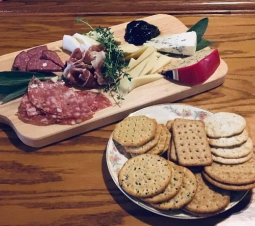 A wooden platter with assorted cheeses, meats, and a small dish of jam, alongside a plate of crackers.