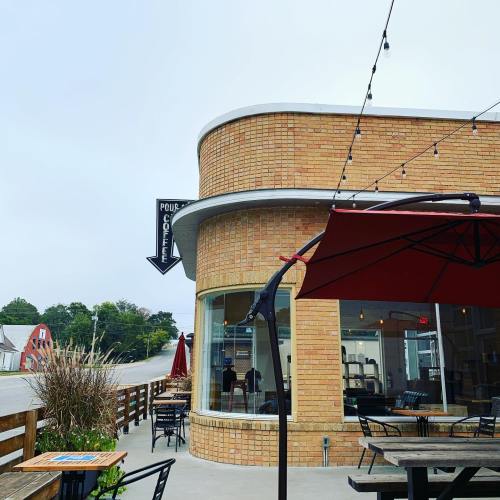 A cozy coffee shop with a brick exterior, outdoor seating, and string lights, set in a rural area.