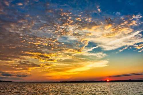A vibrant sunset over a calm body of water, with colorful clouds reflecting the warm hues of the sky.