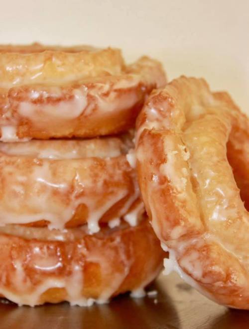 A stack of glazed donuts with a shiny icing coating, showcasing their fluffy texture and golden-brown color.