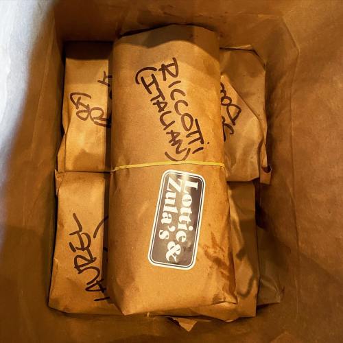 A brown paper bag containing several wrapped items labeled with names, including "Ricotta" and "Laurel."
