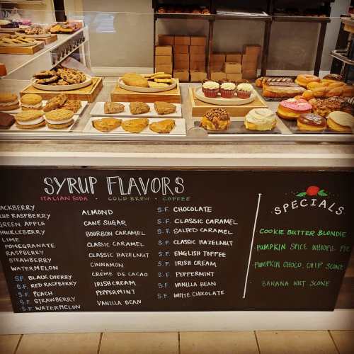 A display of pastries and a chalkboard menu featuring syrup flavors and specials at a café.