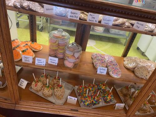 A display case filled with various baked goods, including cookies, candy apples, and colorful treats.