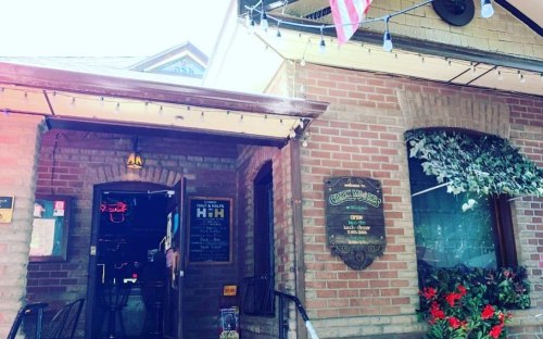 A brick building with a sign for a restaurant, featuring outdoor seating and decorative lights. An American flag hangs above.