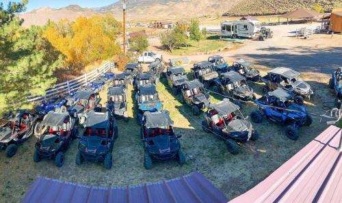 Aerial view of a parking area filled with numerous off-road vehicles, surrounded by trees and mountains.