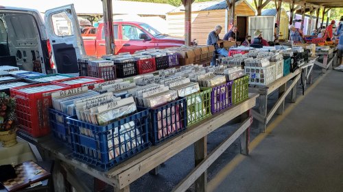 A market scene with tables filled with colorful crates of vinyl records, shoppers browsing in the background.