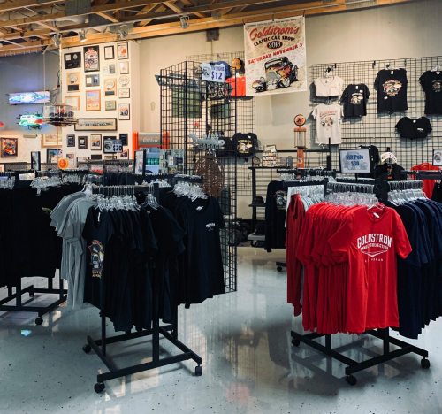 A retail space displaying racks of T-shirts in various colors, with wall decor and memorabilia in the background.