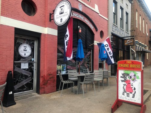Exterior of Engine House restaurant with flags, outdoor seating, and a colorful sign featuring a cartoon character.