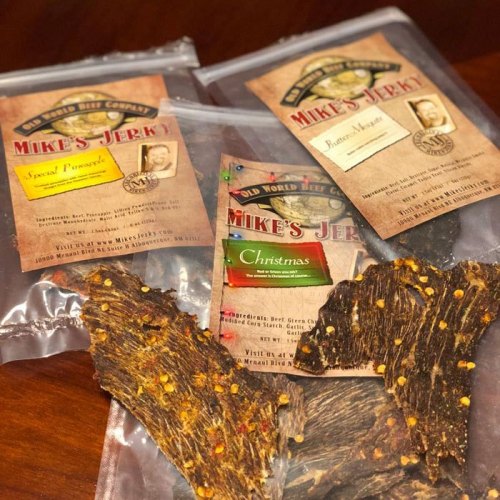 Four bags of Mike's Jerky featuring different flavors, including Special Pineapple and Christmas, with jerky pieces displayed.