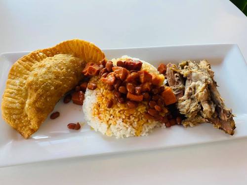 A plate featuring rice with beans, a fried pastry, and shredded meat, arranged neatly on a white dish.
