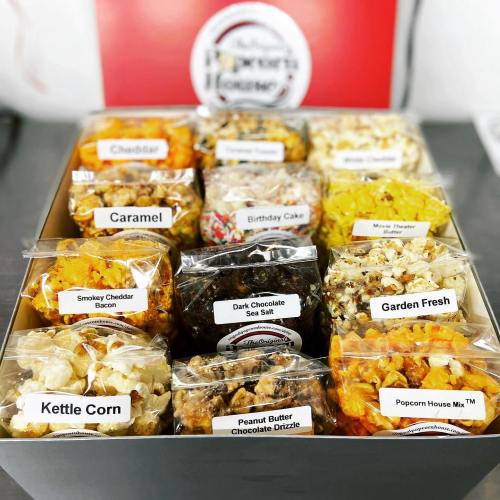 A box of assorted popcorn flavors, including cheddar, caramel, birthday cake, and more, neatly packaged in clear bags.