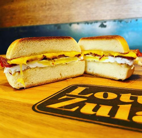 A close-up of a toasted sandwich filled with bacon, cheese, and egg, displayed on a wooden surface.