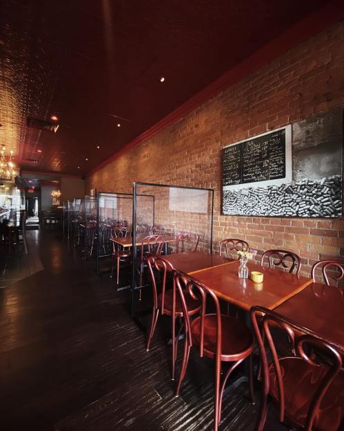 Interior of a restaurant featuring wooden tables, red chairs, and glass partitions, with exposed brick walls and a chalkboard.