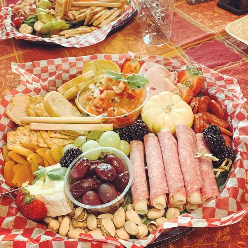 A colorful charcuterie board with meats, cheeses, fruits, and crackers arranged on a red checkered platter.