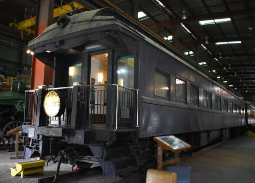 A vintage train car displayed in a museum, featuring a black exterior and large windows.