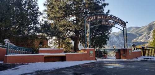 Entrance to Cliff Dwelling Museum, surrounded by trees and mountains, with a light dusting of snow on the ground.