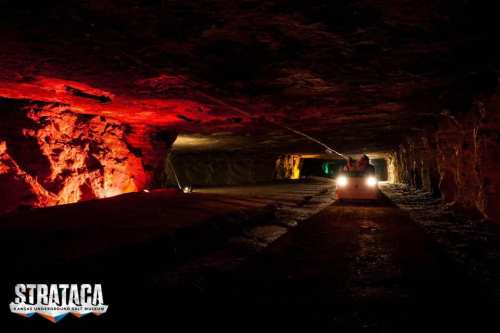 A dimly lit underground salt mine with colorful lights and a small vehicle on the track.
