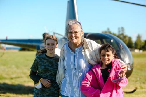 A smiling woman stands with two girls in front of a helicopter on a sunny day.