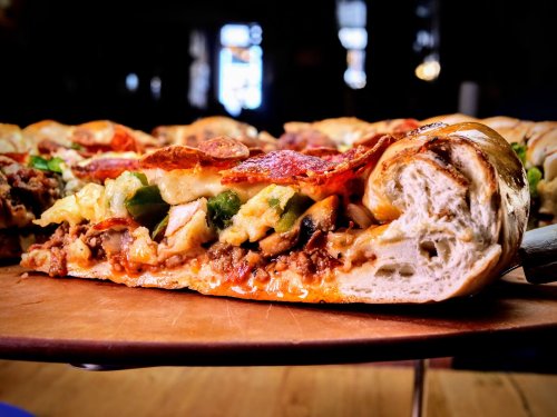 A close-up of a stuffed pizza, showcasing layers of cheese, meats, and vegetables in a golden-brown crust.