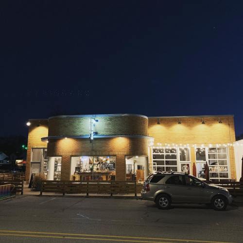 A cozy building at night, illuminated by string lights, with large windows and a parked car in front.