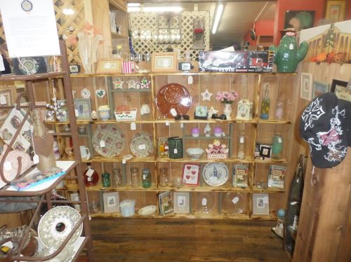 A wooden display shelf filled with various vintage items, including glassware, decorative plates, and framed pictures.