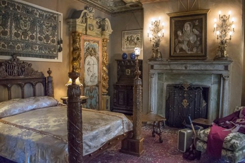 A vintage bedroom with ornate furniture, a fireplace, and decorative wall art, creating a cozy, historical atmosphere.