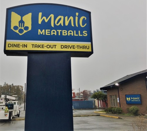 Sign for Manic Meatballs featuring dine-in, take-out, and drive-thru options, set in a rainy outdoor environment.