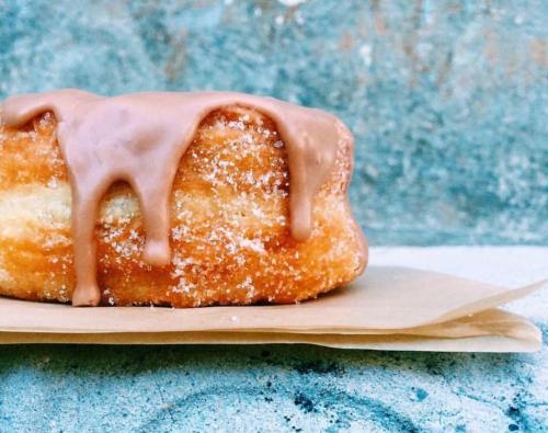 A glazed donut with chocolate icing, resting on a piece of parchment paper against a textured background.